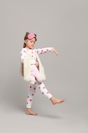 Girl in pajamas and sleep mask with toy bunny sleepwalking on gray background