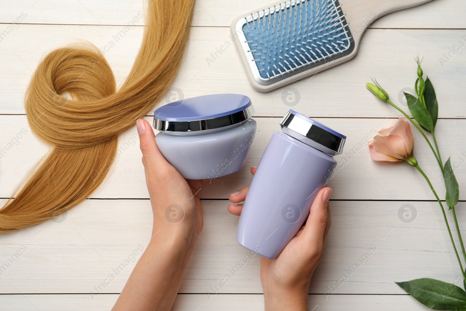 Photo of Woman holding hair care cosmetic products at white wooden table, top view