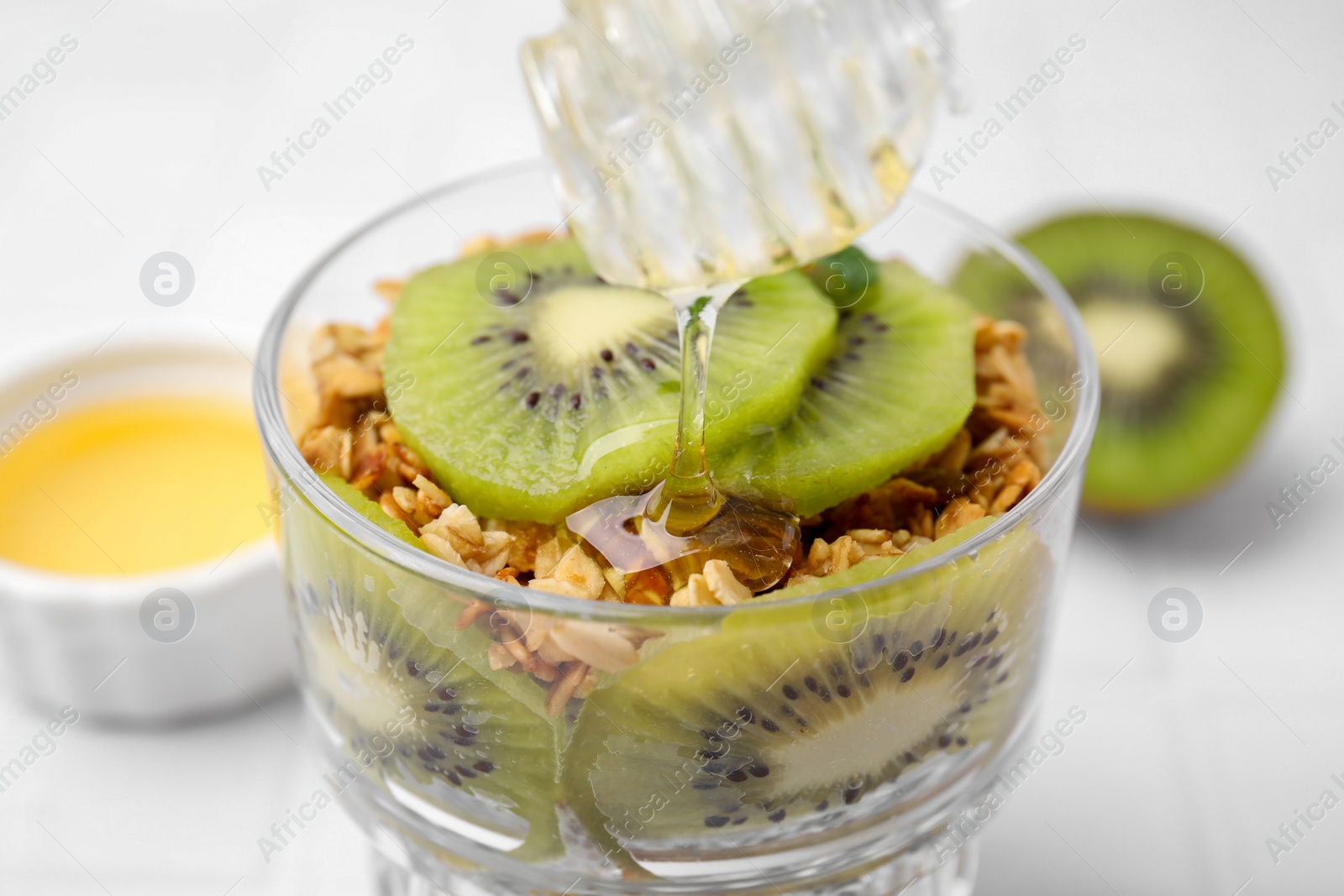 Photo of Pouring honey from onto delicious dessert with kiwi and muesli, closeup