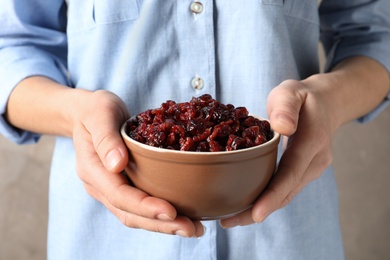 Woman holding bowl with tasty cranberries on color background, closeup. Dried fruits as healthy snack