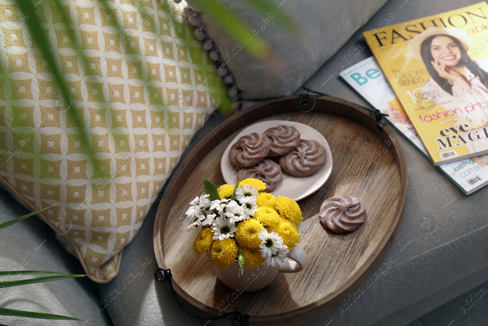 Photo of Tray with flowers in cup and delicious cookies on sofa indoors