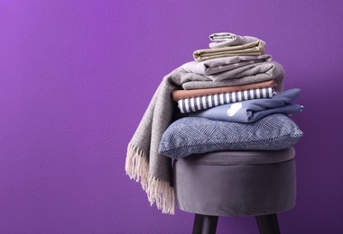 Stack of clean bed sheets and pillow on stool against purple background. Space for text