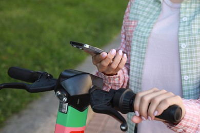 Photo of Woman using smartphone to pay and unblock electric kick scooter outdoors, closeup