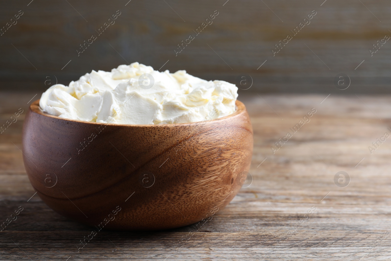 Photo of Bowl of tasty cream cheese on wooden table, space for text