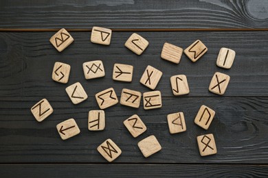 Photo of Runes with different symbols on black wooden table, flat lay