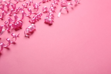 Photo of Shiny serpentine streamers on pink background, space for text