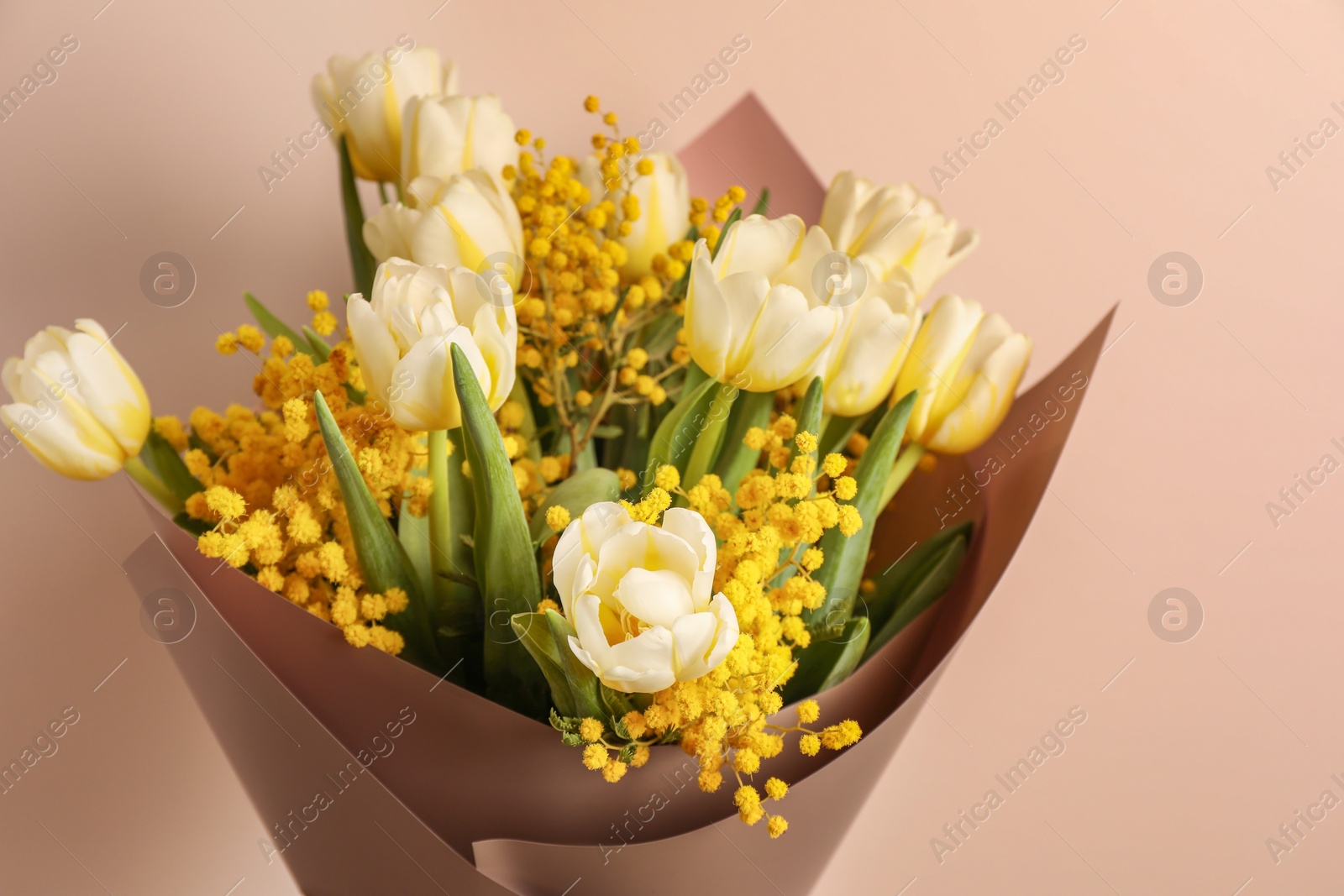 Photo of Bouquet of beautiful spring flowers near beige wall, closeup