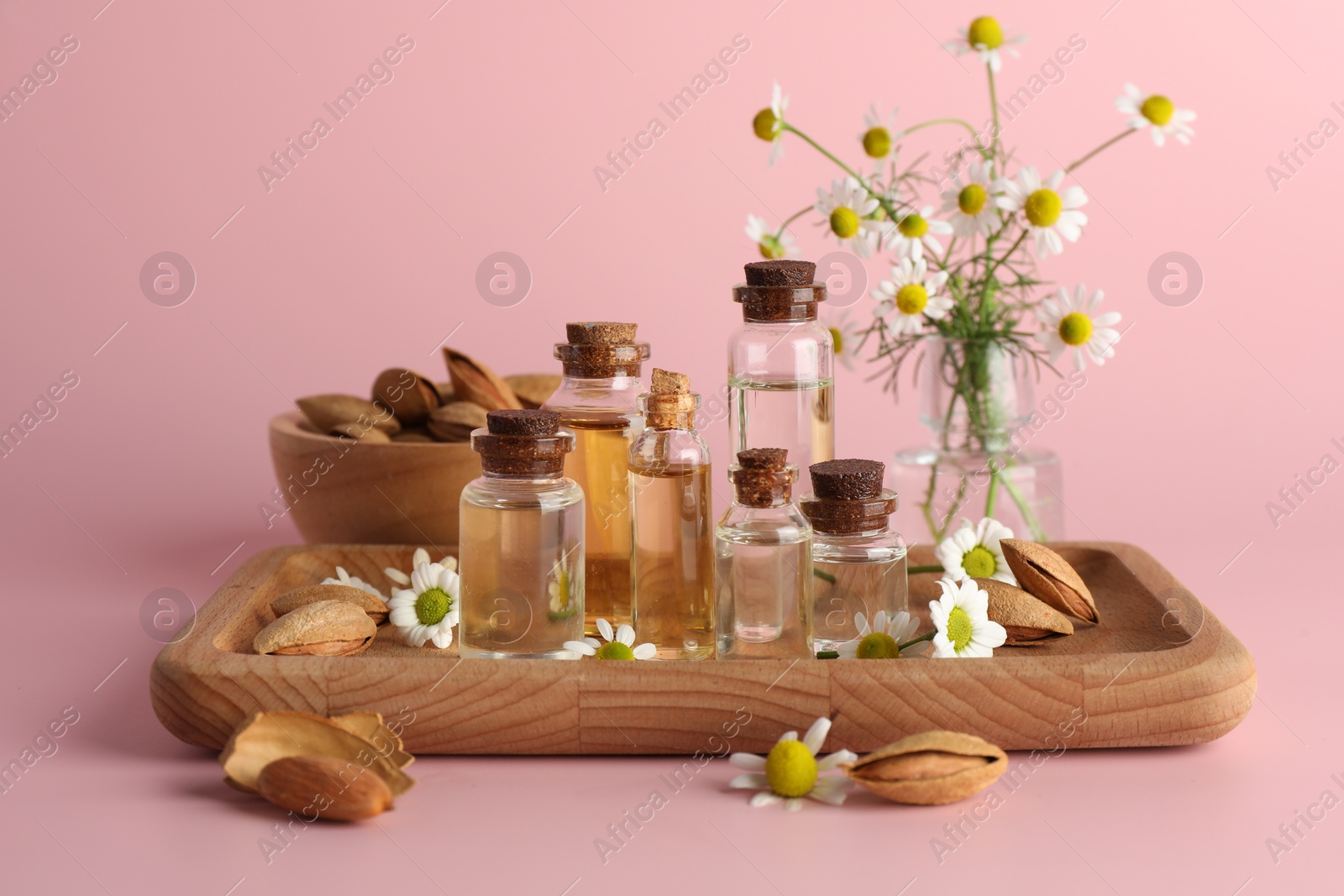 Photo of Aromatherapy. Different essential oils, flowers and almonds on pink background