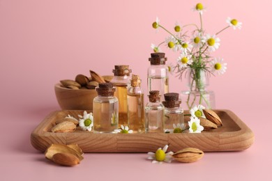 Aromatherapy. Different essential oils, flowers and almonds on pink background