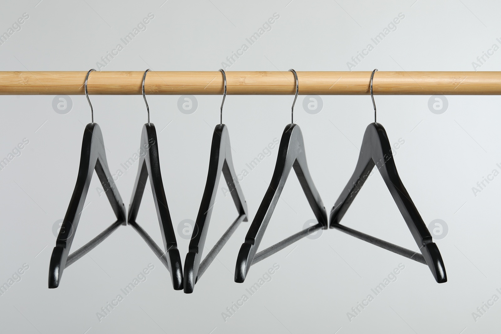 Photo of Black clothes hangers on wooden rack against light grey background