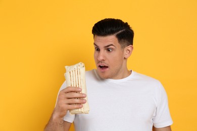 Emotional man with delicious shawarma on yellow background