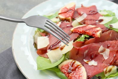 Photo of Eating delicious bresaola salad at grey table, closeup