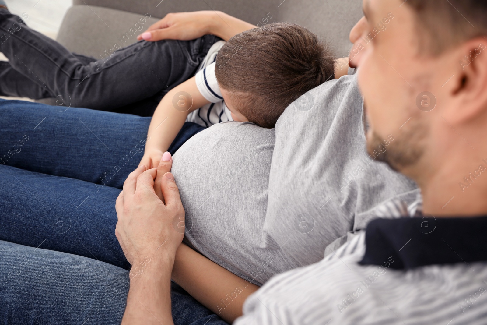 Photo of Pregnant mother, father and son spending time together on sofa at home. Family time