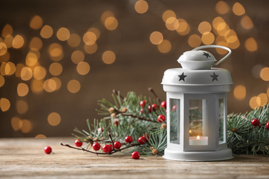 Photo of Composition with lantern and decorated fir branches on table against blurred background. Winter holidays