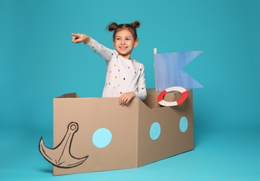 Cute little girl playing with cardboard boat on color background