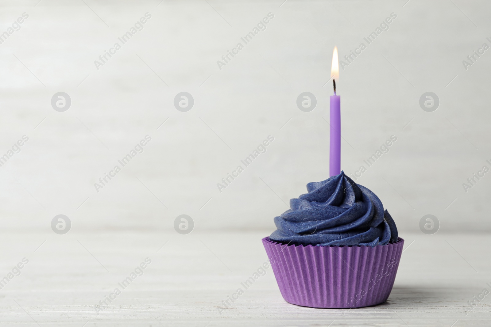 Photo of Delicious birthday cupcake with cream and burning candle on white wooden table. Space for text