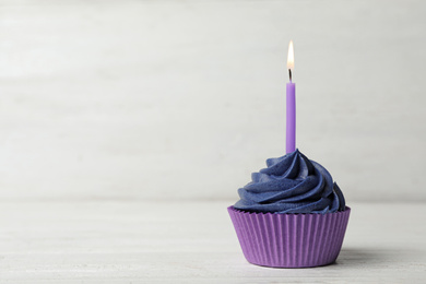 Photo of Delicious birthday cupcake with cream and burning candle on white wooden table. Space for text