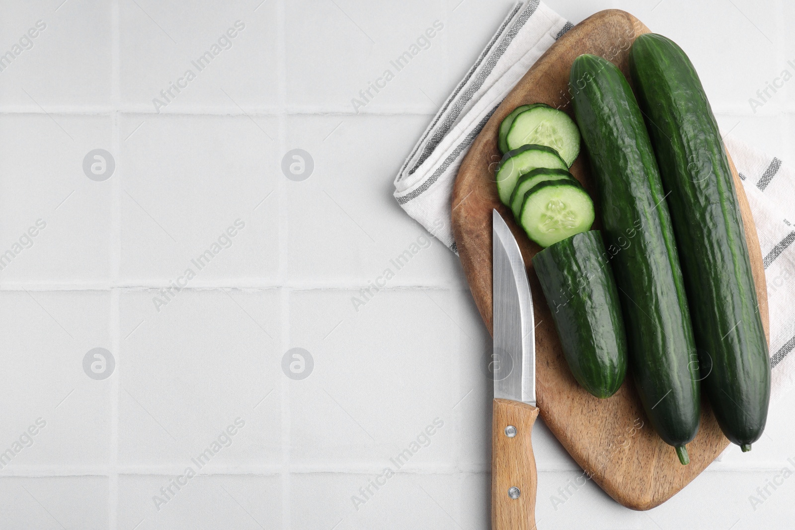 Photo of Fresh cucumbers and knife on white tiled table, top view. Space for text