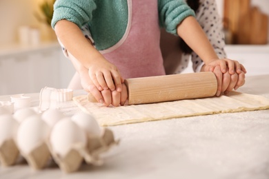 Photo of Mother and daughter rolling out dough in kitchen at home, closeup