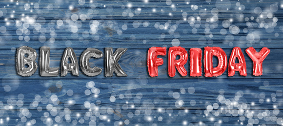 Phrase BLACK FRIDAY made of foil balloon letters on blue wooden background. Banner design