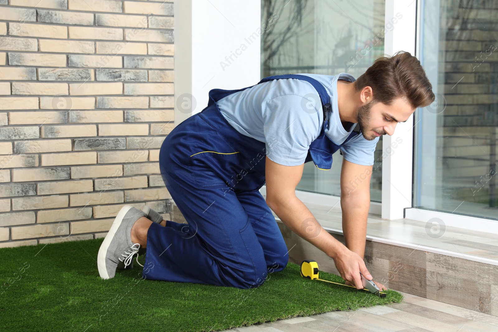 Photo of Man in uniform cutting artificial grass carpet indoors