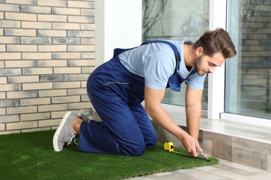 Man in uniform cutting artificial grass carpet indoors