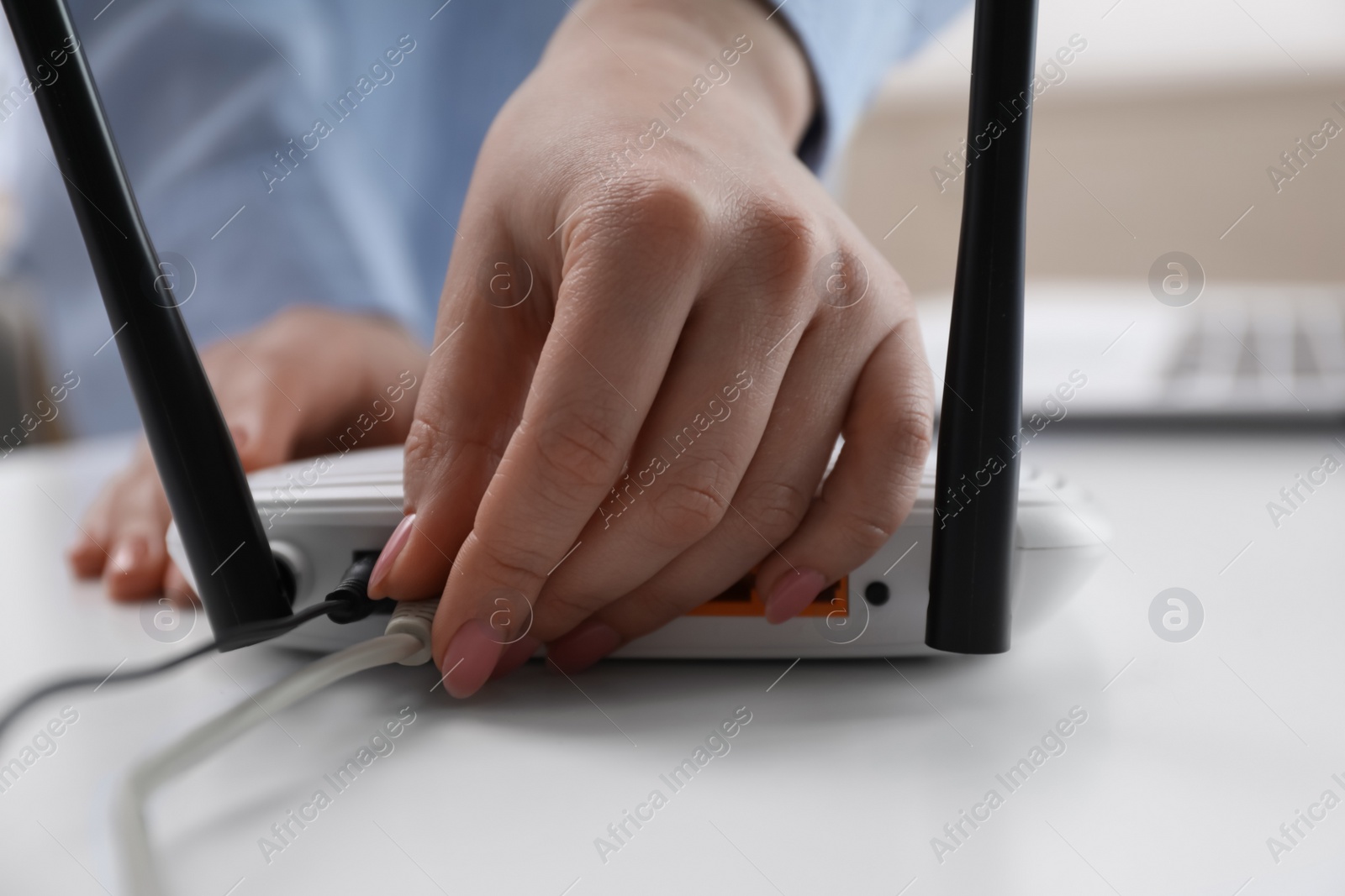 Photo of Woman connecting cable to router at white table, closeup. Wireless internet communication