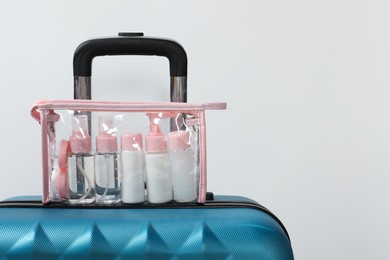 Photo of Cosmetic travel kit in plastic bag on suitcase against light background, space for text