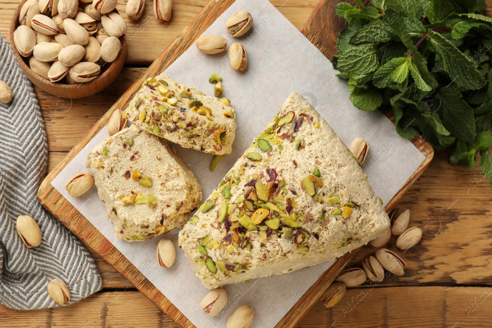 Photo of Tasty halva with pistachios and mint on wooden table, flat lay