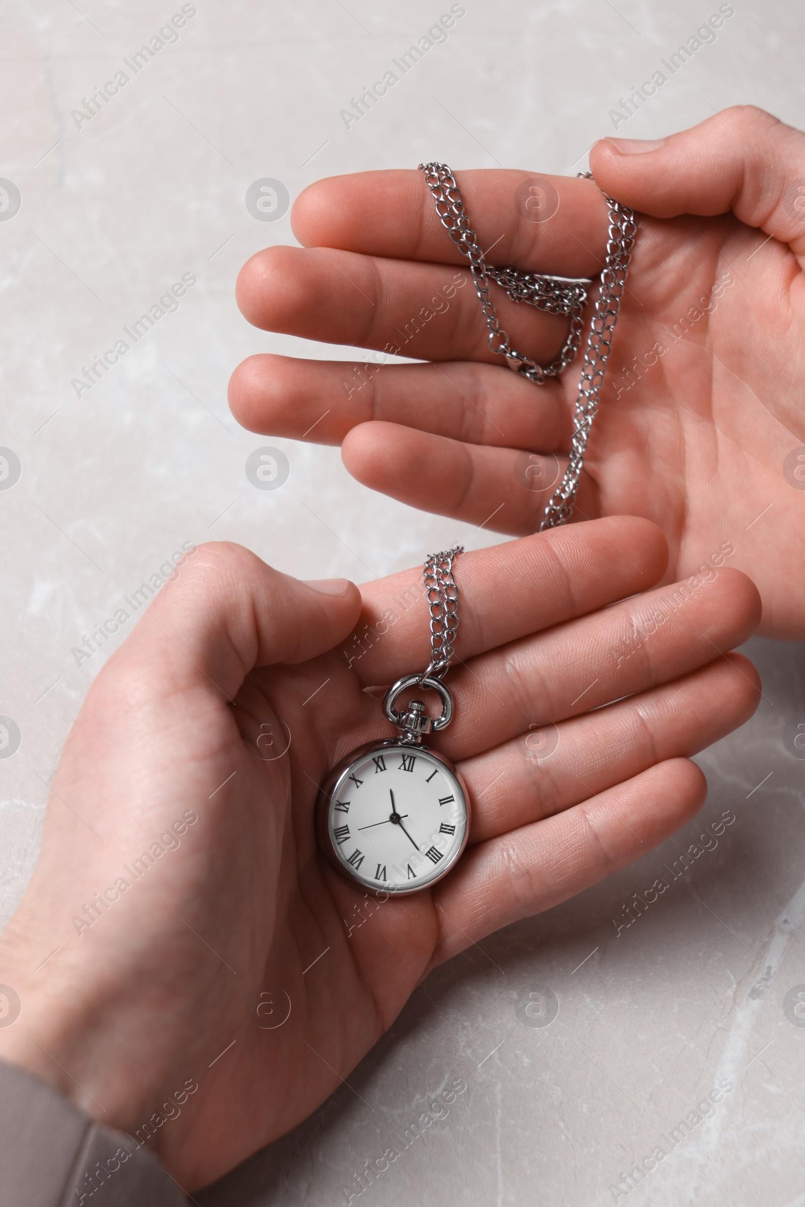 Photo of Man holding chain with elegant pocket watch at light marble table, closeup