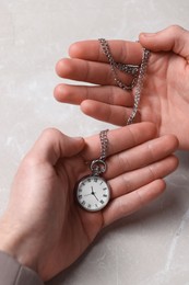 Man holding chain with elegant pocket watch at light marble table, closeup