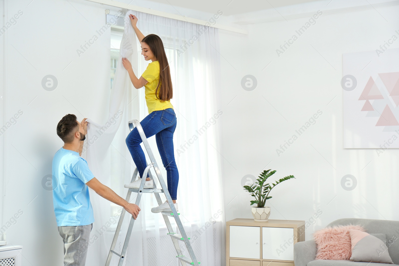Photo of Young couple hanging window curtain in room. Space for text