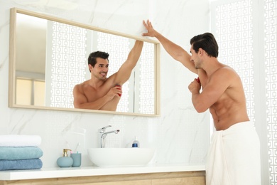 Handsome young man applying deodorant in bathroom