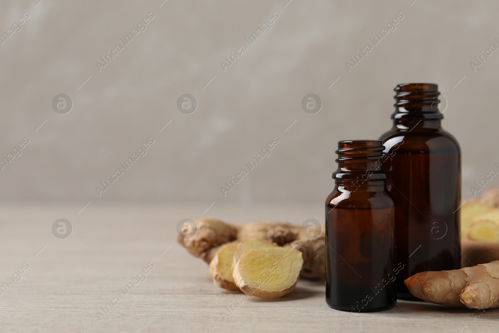 Photo of Glass bottles of essential oil and ginger root on beige wooden table, space for text