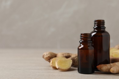 Photo of Glass bottles of essential oil and ginger root on beige wooden table, space for text