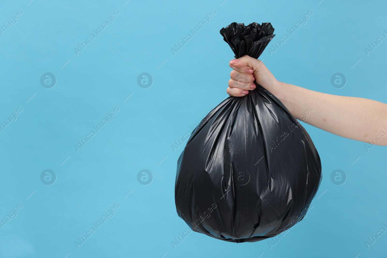 Photo of Woman holding plastic bag full of garbage on light blue background, closeup. Space for text