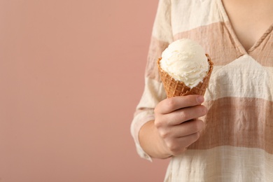 Woman holding white ice cream in wafer cone on pink background, closeup. Space for text