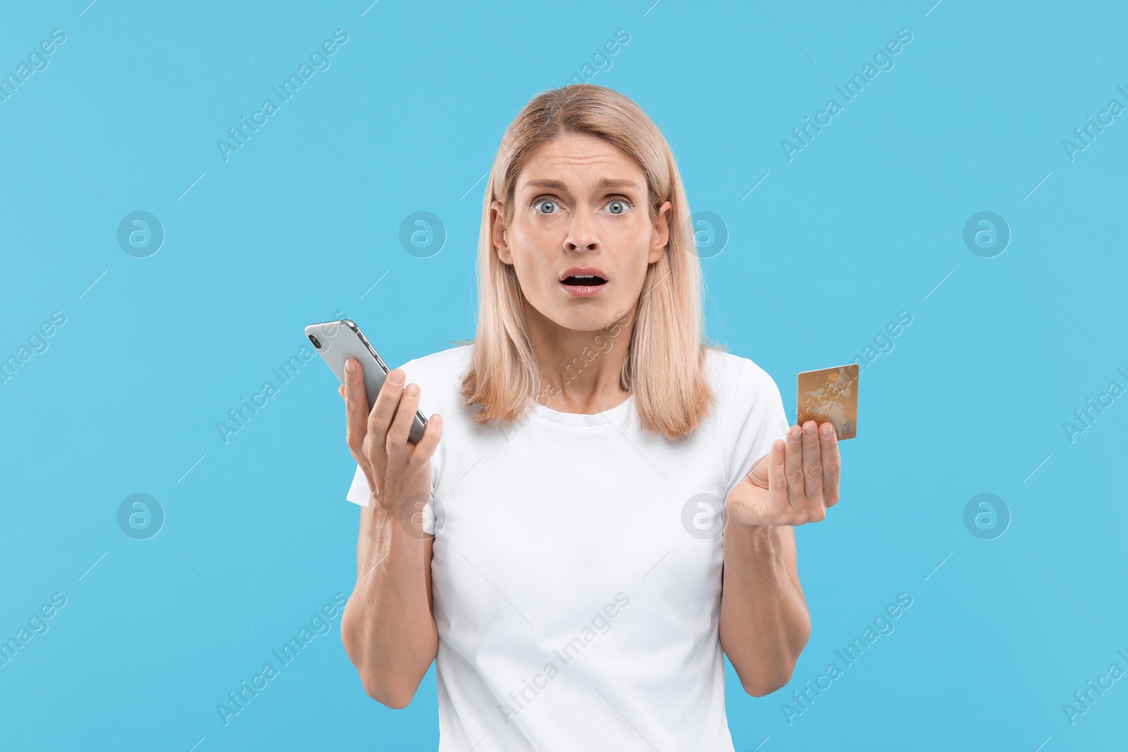 Photo of Stressed woman with credit card and smartphone on light blue background. Be careful - fraud