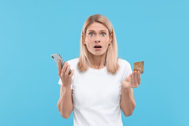 Photo of Stressed woman with credit card and smartphone on light blue background. Be careful - fraud