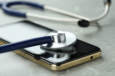 Modern smartphone and stethoscope on grey table, closeup