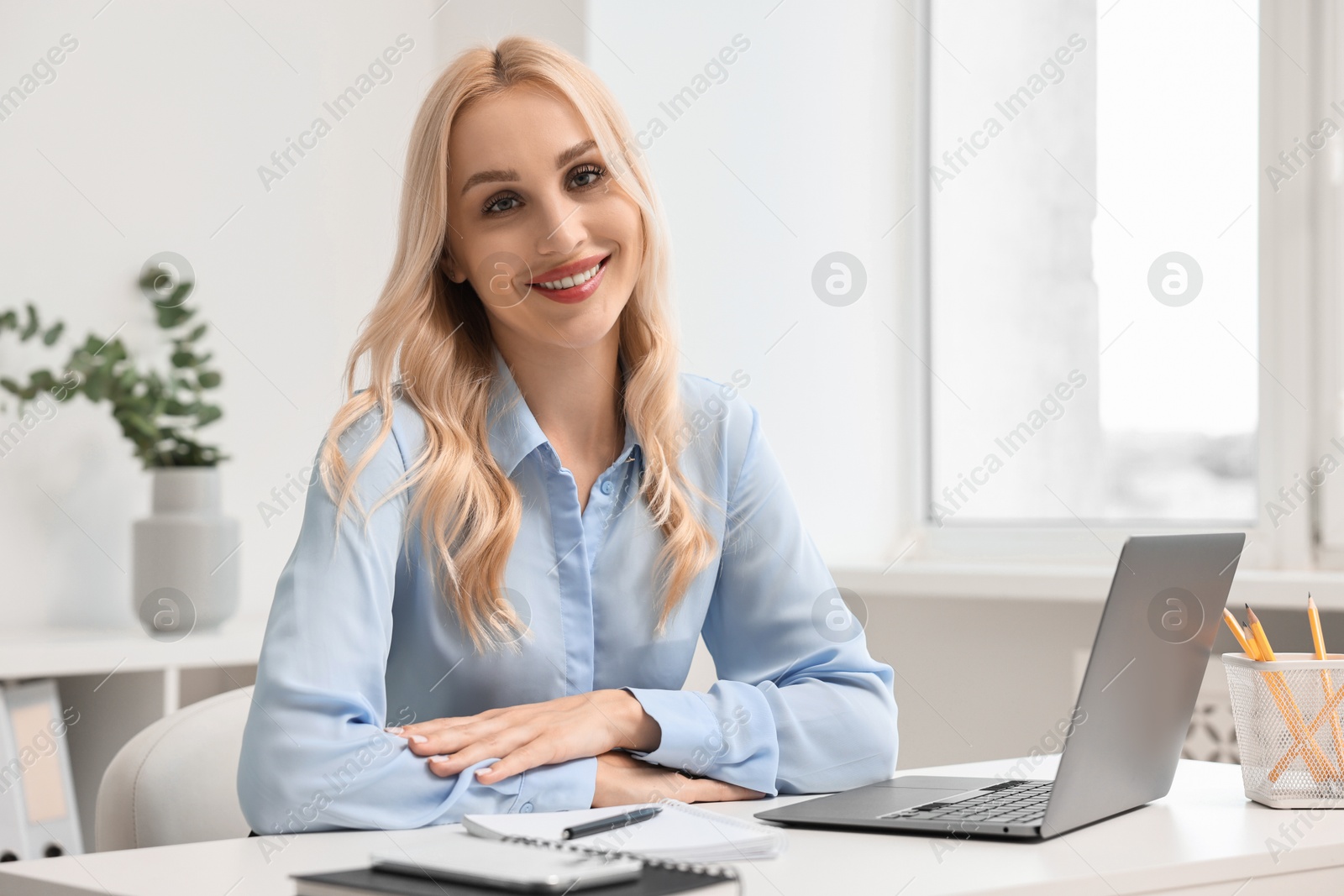 Photo of Happy secretary at table with laptop and stationery in office