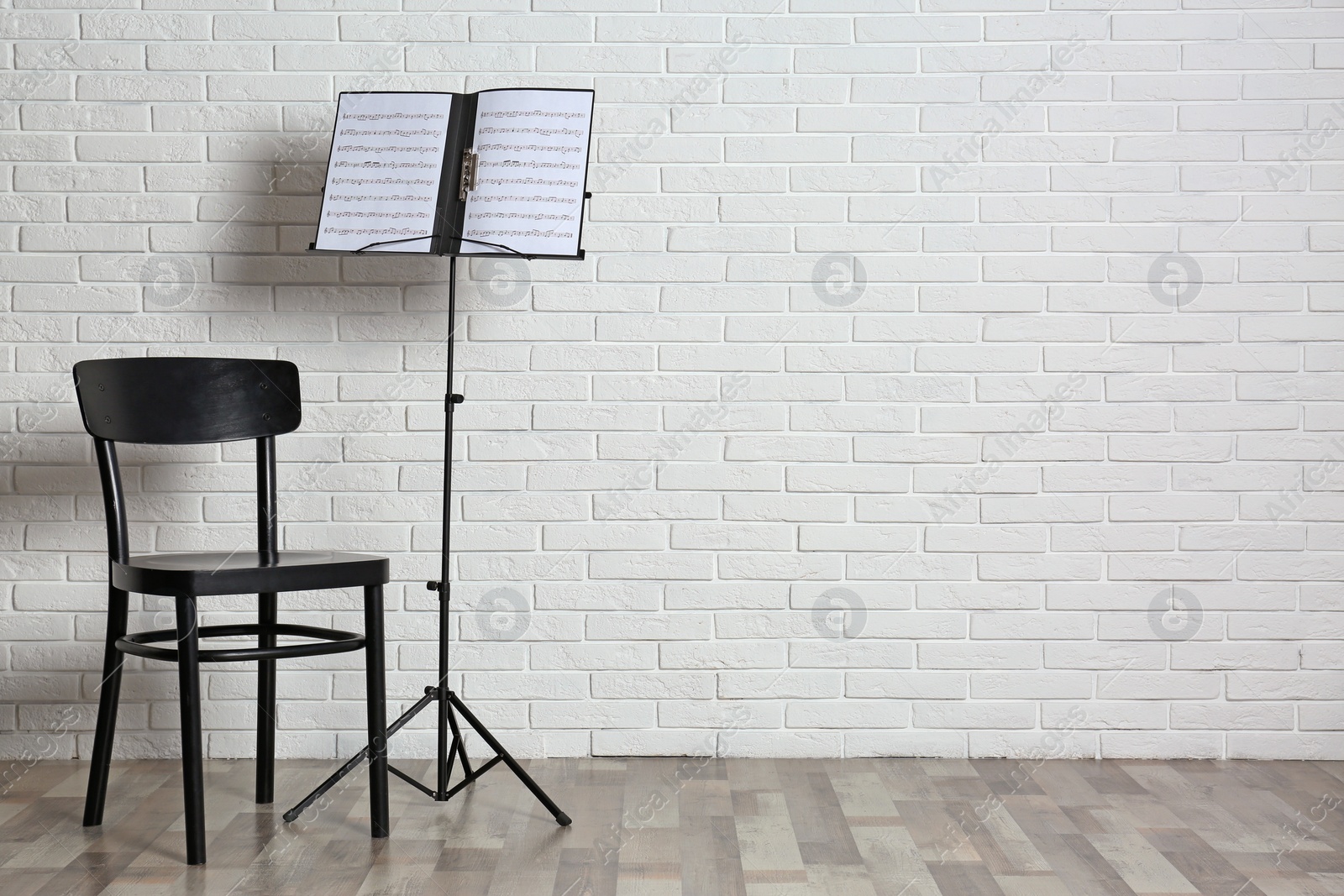 Photo of Chair and note stand with music sheets near brick wall. Space for text