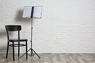 Chair and note stand with music sheets near brick wall. Space for text