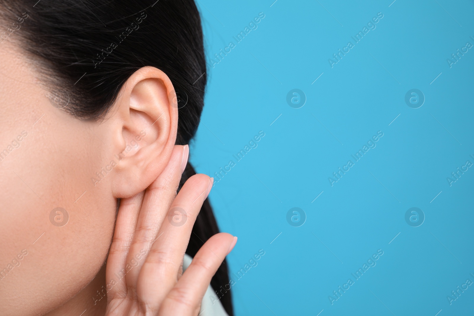 Photo of Woman showing hand to ear gesture on light blue background, closeup. Space for text