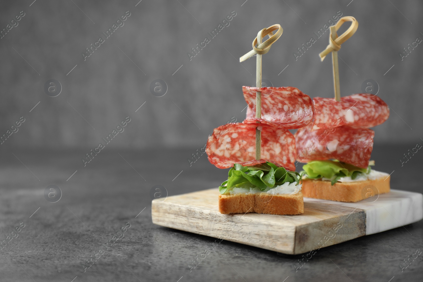 Photo of Tasty canapes with salami, greens and cream cheese on grey table, closeup. Space for text