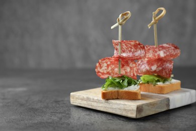 Photo of Tasty canapes with salami, greens and cream cheese on grey table, closeup. Space for text
