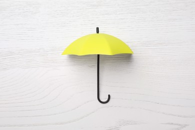 Photo of Small yellow umbrella on white wooden background, top view