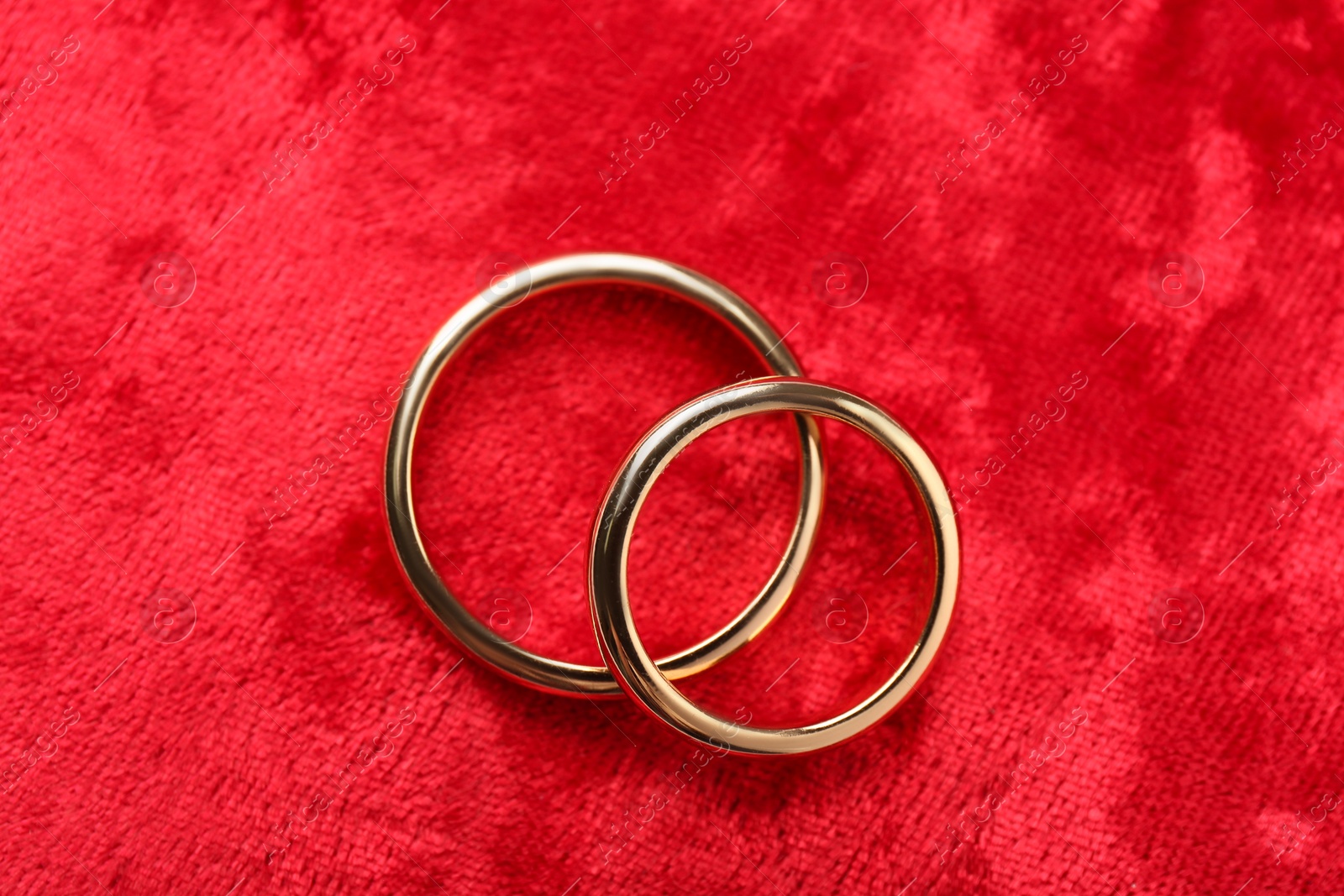 Photo of Honeymoon concept. Two golden rings on red velvet, top view