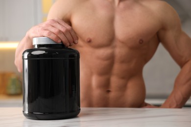 Photo of Young man with jar of protein powder at white marble table in kitchen, closeup