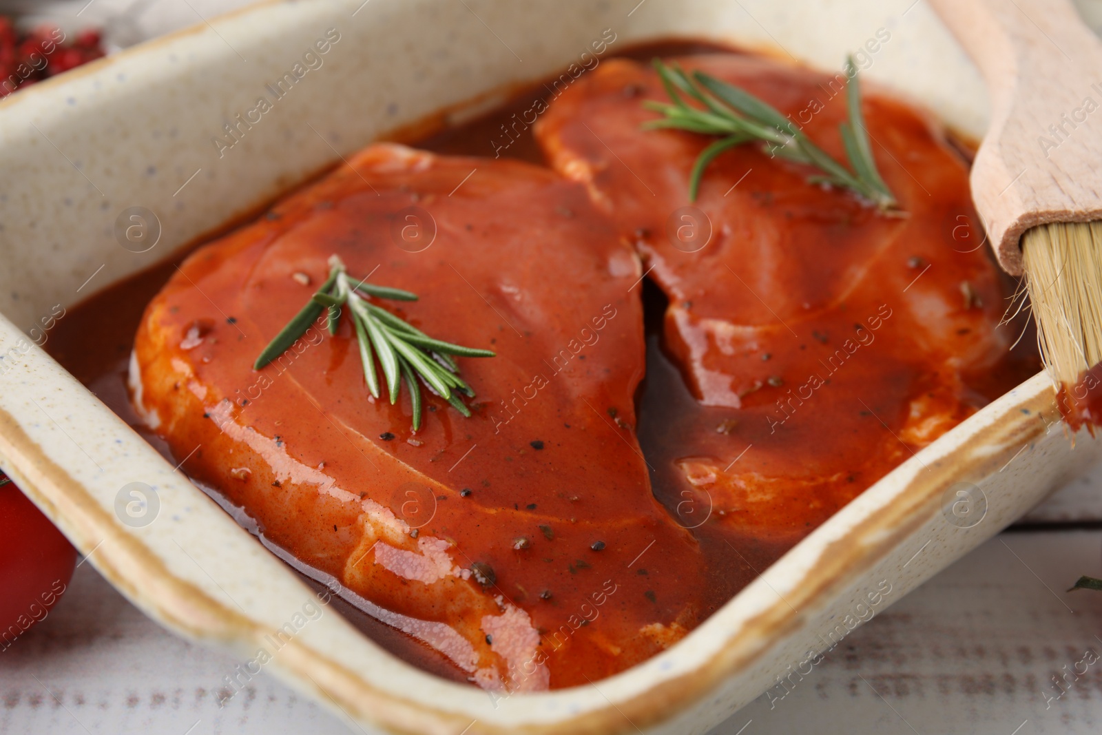 Photo of Raw marinated meat and rosemary in baking dish on white wooden table, closeup